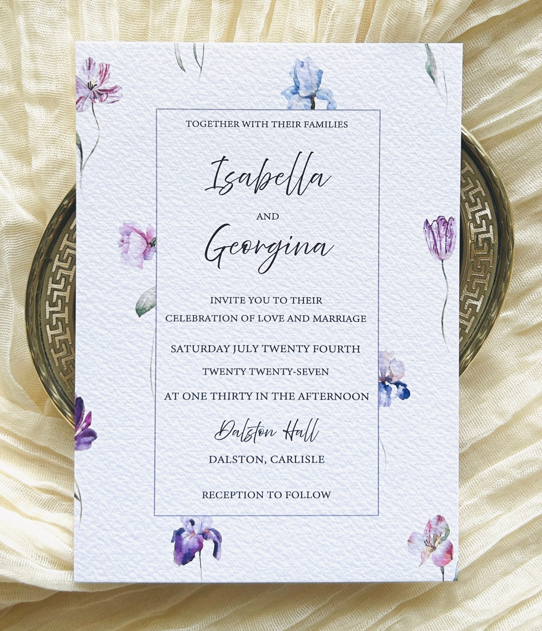 Wedding invitation card with blue, pink and purple floral design on a textured surface
