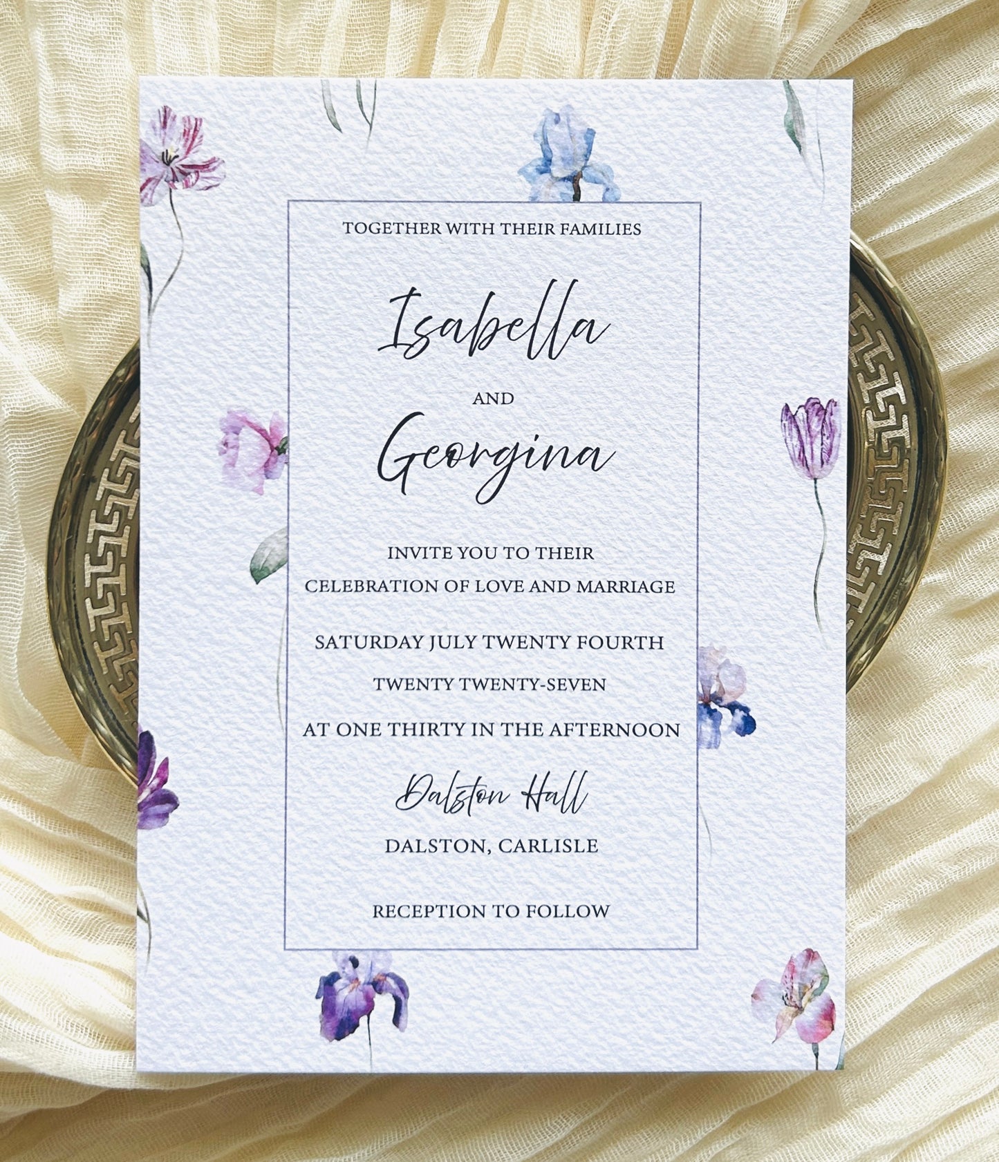 Wedding invitation card with blue, pink and purple floral design on a textured surface
